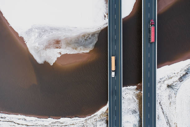 Trucking In Winter Aerial drone view of semi trucks crossing a tidal river. bridge built structure photos stock pictures, royalty-free photos & images