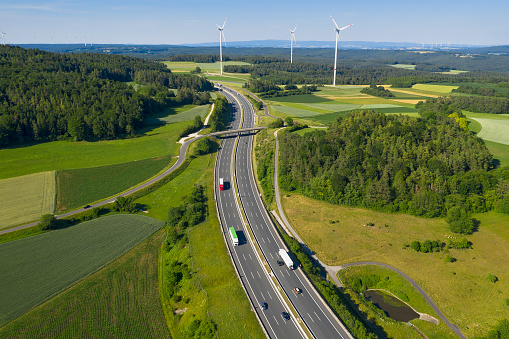 Multiple lane highway with trucks in rural area, wind turbines in the background, bird's eye view.
