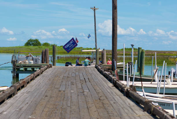 A "Trump 2020" Flag Stands Out on a Passing Fishing Boat, Tangier Island, Virginia Tangier Island, Virginia / USA - June 21, 2020: A multi-generational family onboard a May-Craft center console boat flying a “Trump 2020” flag passes a wooden dock in this popular tourist destination in the Chesapeake Bay. tangier island stock pictures, royalty-free photos & images