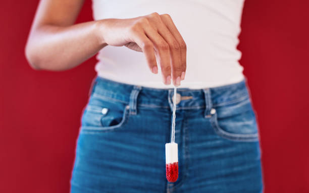 Studio shot of an unrecognizable woman holding a used tampon against a red background