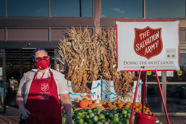 Tulsa USA Masked Woman collecting money for The Salvation Army stands by pile of pumpkins and gourds and ornamental straw with sign and bucket outside store stock photo