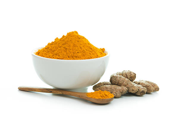 Tumeric powder in a white bowl with wooden spoon Bowl of turmeric powder with fresh turmeric root curry powder stock pictures, royalty-free photos & images