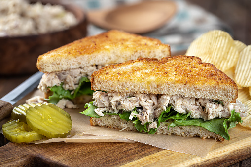 Tuna salad sandwich with lettuce on toasted whole grain bread cut in half on a cutting board