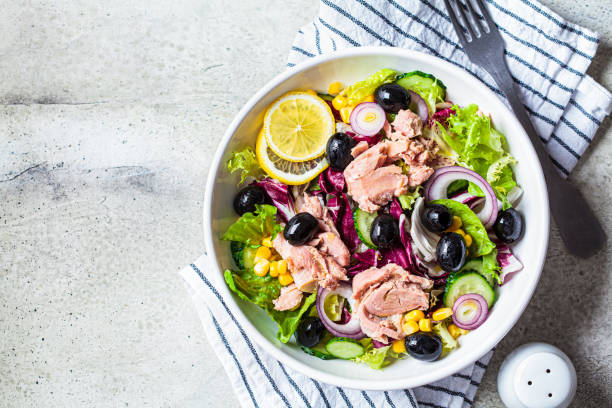 Tuna salad with cucumbers, corn, olives and red onions in white bowl, top view. Comfort food concept. stock photo