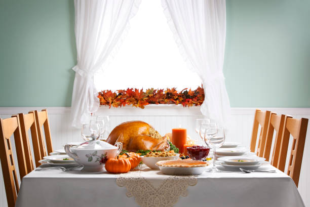 Turkey As Centerpiece For A Thanksgiving Feast A Thanksgiving turkey sits ready to be carved for a Thanksgiving Day feast on a festively decorated dining room table.  The side items include pumpkin pie, stuffing, steamed vegetables, and cranberry sauce. Light streams in through a window in the background adorned with an autumn leaf garland. dining table stock pictures, royalty-free photos & images