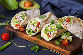 Turkey wraps with avocado, tomatoes and iceberg lettuce on chopping board. Tortilla, burritos, sandwiches, twisted rolls