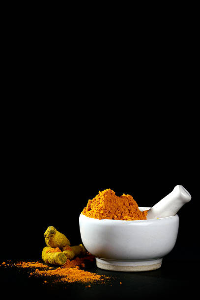 Turmeric powder in mortar with pestle and roots stock photo