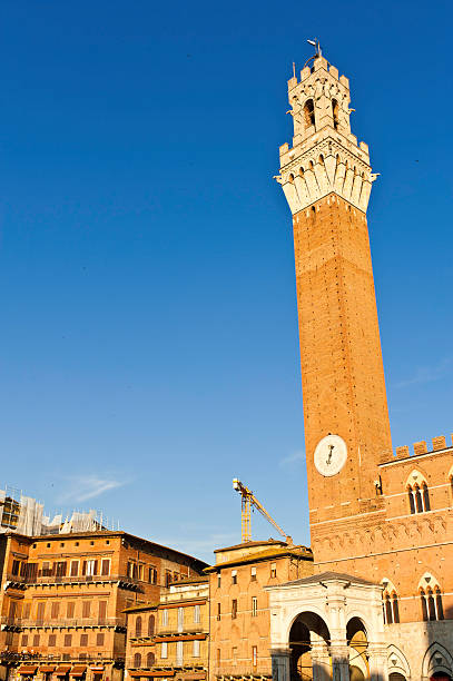 Tuscany Siena Il Campo Torre del Mangia Palazzo Pubblico Italy The busy restaurants and shops of the historic palazzi signorili surrounding the Piazza del Campo, home to the famous Palio horse race, overlooked by the iconic spire of the Torre del Mangia high above the Palazzo Pubblico under deep blue Tuscan skies, Siena, Italy. ProPhoto RGB profile for maximum color fidelity and gamut. siena festival il campo stock pictures, royalty-free photos & images