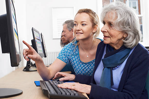 Tutor Helping Senior Woman In Computer Class Tutor Helping Senior Woman In Computer Class computer equipment stock pictures, royalty-free photos & images