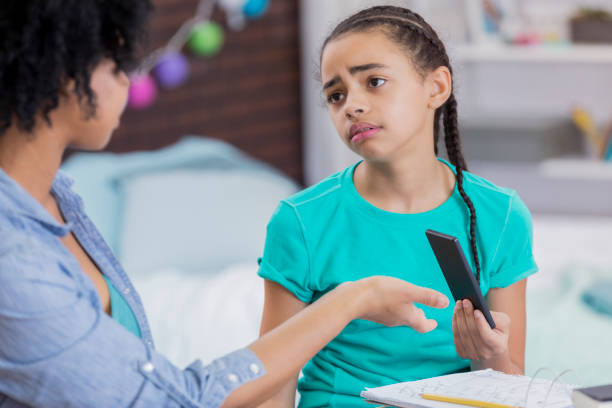 Tween girl hands her phone over to her mother African American mom punishes daughter by taking away the girl's phone. The girl has a sad expression while handing over the phone. disciplining a child stock pictures, royalty-free photos & images