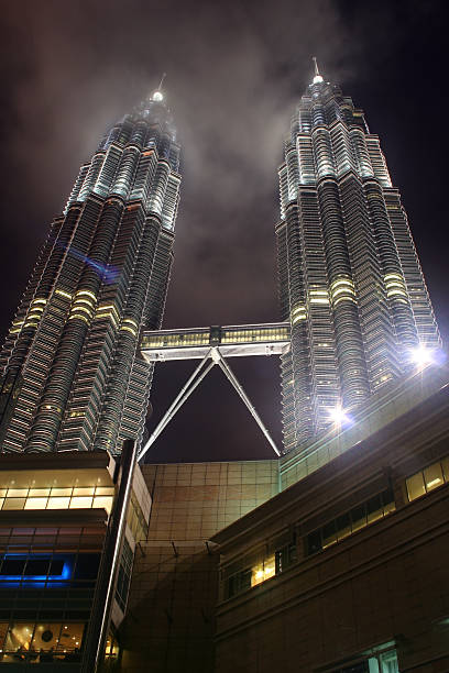 Twin Towers At Night Petronas Twin Towers in Kuala Lumpur, Malaysia, lighting up the sky on a cloudy night. central market kuala lumpur stock pictures, royalty-free photos & images