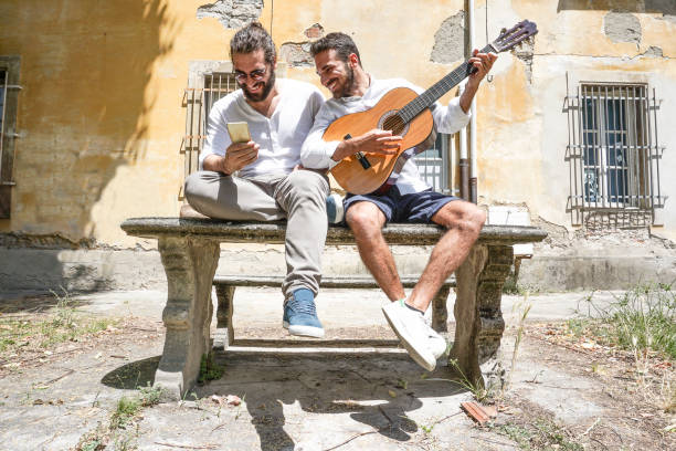 Two adult men playing guitar and using the phone stock photo