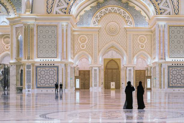 deux femmes arabes de la région vêtues de noir traditionnel visitant la grande salle du nouveau palais présidentiel majestueux, qasr al watan, avec une équipe de gardes de sécurité sur fond flou. - femme musulmane abaya photos et images de collection