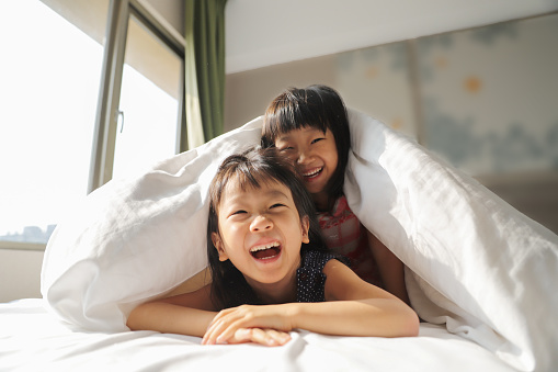 two smiling Asian girls playing quilt on the bed.