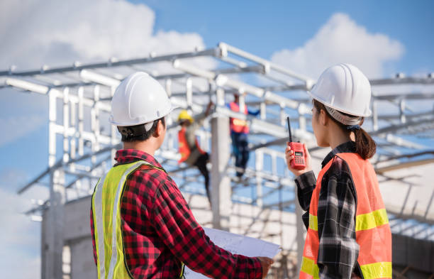 Two Asian man and woman engineer wears white safety helmet stand hold blueprint and radio while checking build in the construction site. stock photo