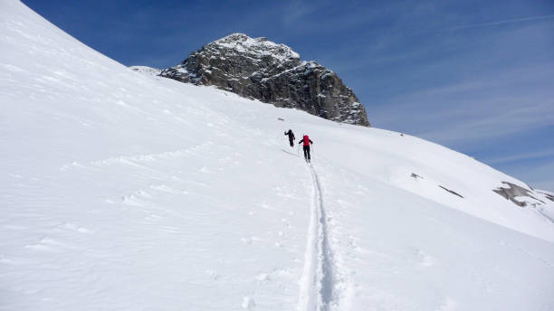 two backcountry skiers hiking to a far away mountain peak in the Austrian Alps in winter two backcountry skiers hiking to a far away mountain peak in the Austrian Alps in winter under a blue sky osttirol stock pictures, royalty-free photos & images