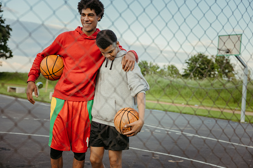 Two basketball players holding balls and embracing on outdoor sports court