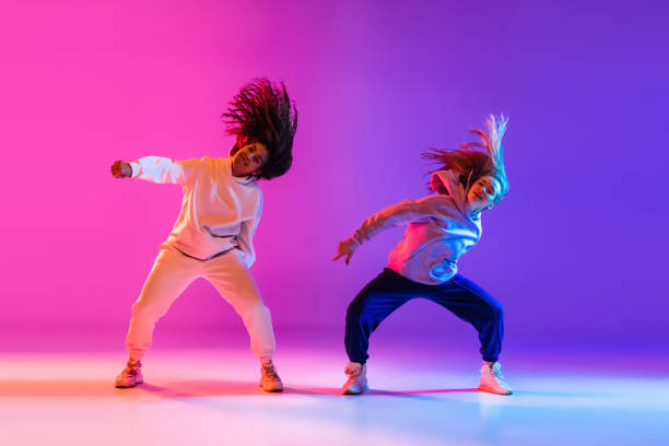 Two beautiful active girls dancing on gradient pink purple neon studio background Stylish two beautiful young girls dancing hip-hop on gradient pink purple neon background. Sport achievement, spirit of expression. Concept of dance, youth, hobby, dynamics, movement, action, ad paint neon color neon light ultraviolet light stock pictures, royalty-free photos & images