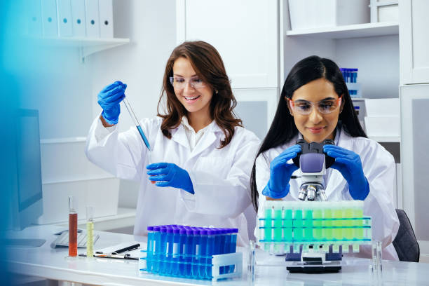 Two beautiful young female scientists working in laboratory with test tubes and microscope doing some research stock photo