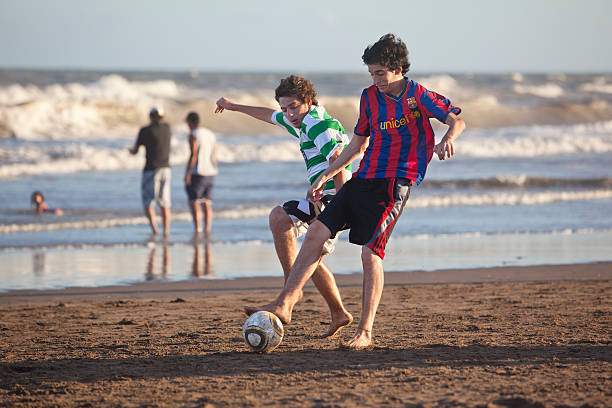 Two boys playing soccer at the beach in Argentina Villa Gesell, Argentina - January 2, 2010: Two adolescents playing soccer on the beach of Villa Gesell at the atlantic coast of Argentina. The red and blue jersey is from the soccer club of Barcelona, Spain. fc barcelona stock pictures, royalty-free photos & images