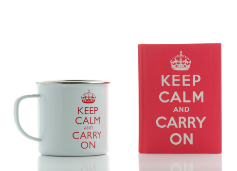 London, England-March 18, 2011.  Two British souvenirs with the famous historical phrase on them to Keep Calm and Carry On.  The souvenirs are a white metal coffee mug and a small red book filled with quotes about keeping calm and carrying on.
