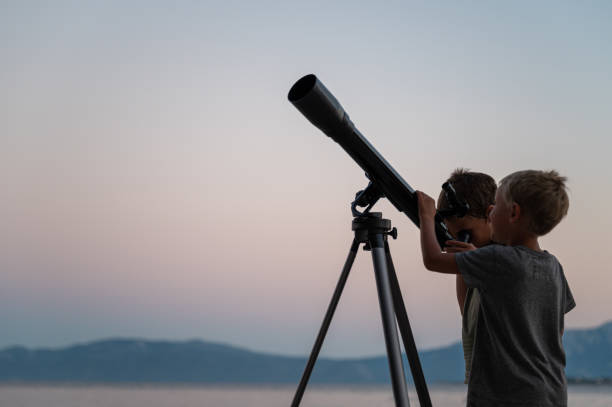 Two brothers looking at the stars using a telescope by the sea stock photo