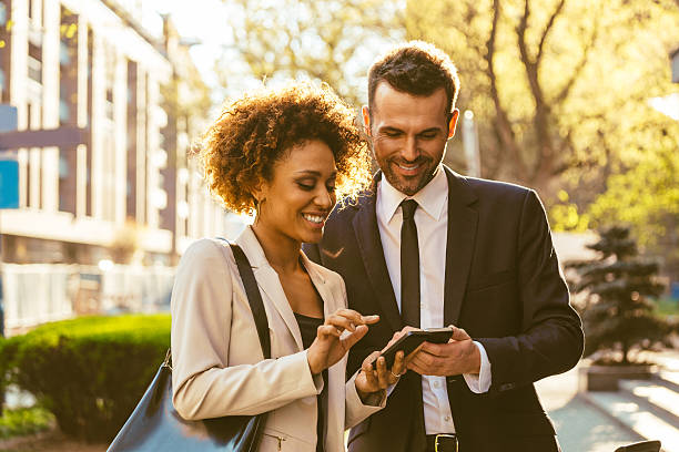 Two business people using smart phones outdoor Outdoor portrait of cheerful businessman and businesswoman using a smart phones. mobile real estate stock pictures, royalty-free photos & images