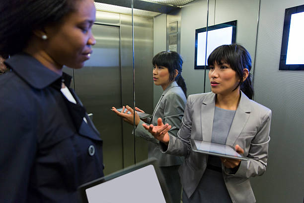 Two business women in elevator discussing,using digital tablets stock photo