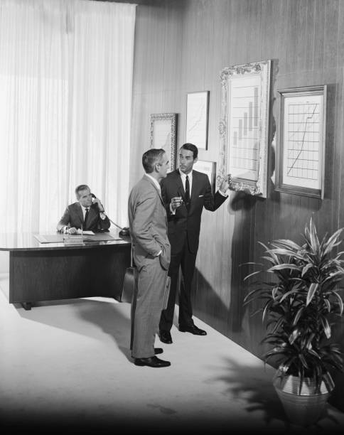 Two businessman discussing at bar chart while another man using telephone in background  1964 stock pictures, royalty-free photos & images