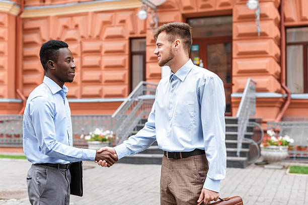 two businessmen  shaking hands African American businessman and a Caucasian businessman shaking hands on the background red buildings in the city second chance stock pictures, royalty-free photos & images
