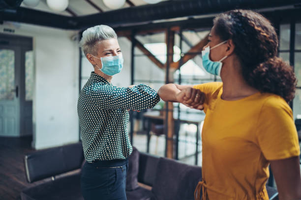 Two businesswomen greeting with elbows Businesswomen with protective masks meeting in the office elbow stock pictures, royalty-free photos & images
