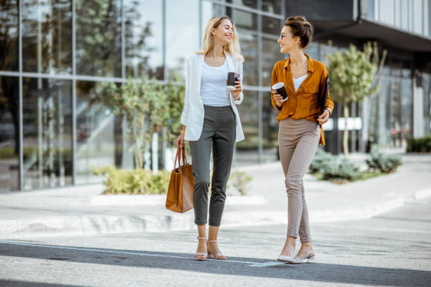 twee zakenvrouwen wandelen buitenshuis - walking with coffee stockfoto's en -beelden