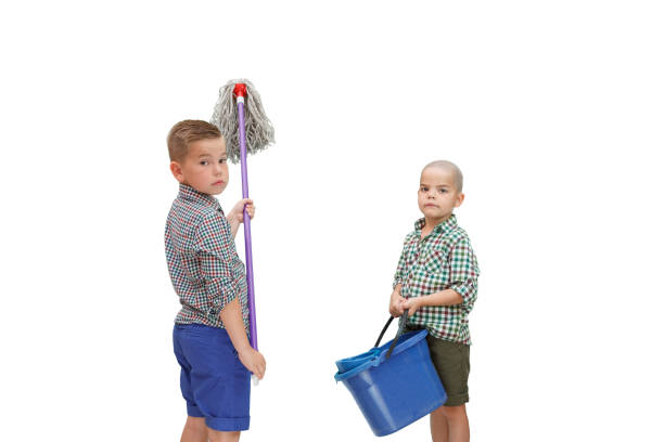two Caucasian boy standing on a white isolated background and holding a bucket of water and a MOP for cleaning stock photo
