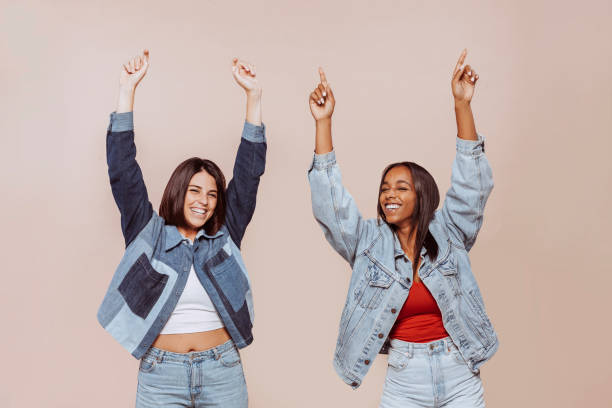 Two cheerful female friends having fun with arms raised up at studio stock photo