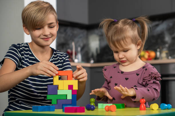 Two children, boy teenager and cute toddler girl playing with toy blocks, building towers at home. stock photo