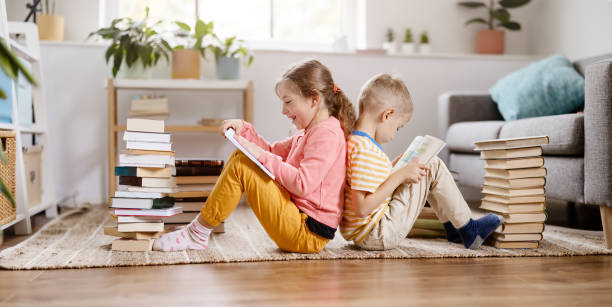 Two children sitting on the floor in the room and reading books stock photo
