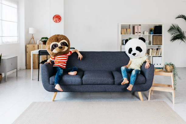 Two children wearing giant animal masks while sitting on the sofa stock photo