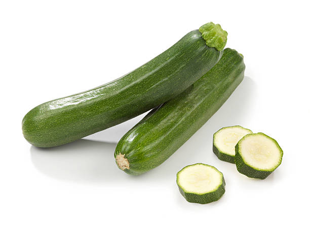 Two courgettes stacked with three slices beside them stock photo