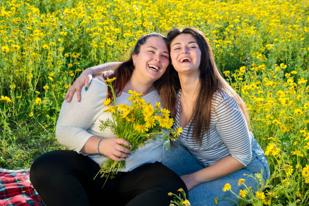 two curvy girls in a field of daisies laugh happy in a daisy field stock photo