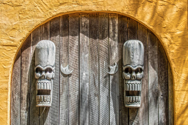 Two decorative tiki god masks hang on boards surrounded by orange stucco arch stock photo