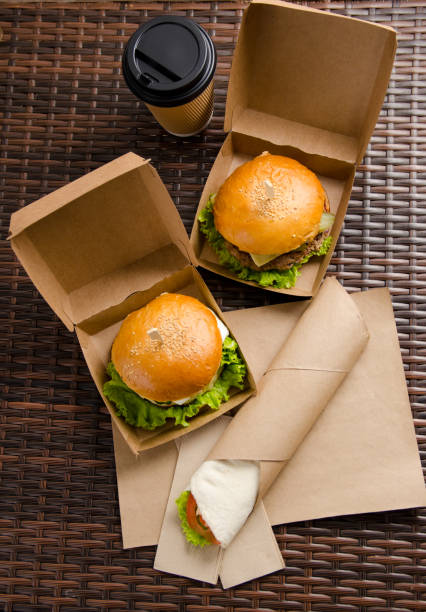 two different burgers in boxes and chicken roll with vegetables on a paper sheet. vertical view two different burgers in boxes and chicken roll with vegetables on a paper sheet. vertical view. burger wrapped in paper stock pictures, royalty-free photos & images