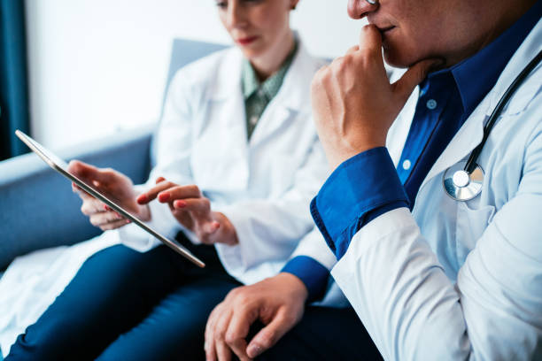 Two doctors having conversation over a case in doctor's office. Shot of a two confident doctors at a meeting. Doctor and nurse sitting on the sofa and discussing over a medical report in doctor's office.  Healthcare staff having discussion in the hospital. Two doctors having discussion about patient diagnosis, using digital tablet. medical technology stock pictures, royalty-free photos & images