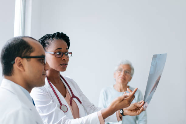 Two doctors looking at x-ray in front of patient Two doctors holding and looking at an x-ray in front of a senior female patient. beautiful haitian women stock pictures, royalty-free photos & images