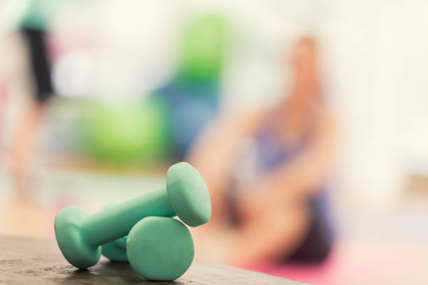 Two dumbbells rest on a table in the foreground Green barbells are stacked on a table at the fitness studio. round dumbbells stock pictures, royalty-free photos & images