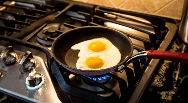 Two eggs being fried in a non-stick skillet on a gas range. stock photo