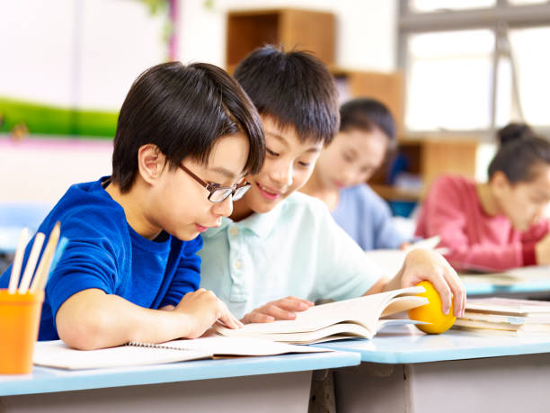 two elementary school students sharing a book stock photo