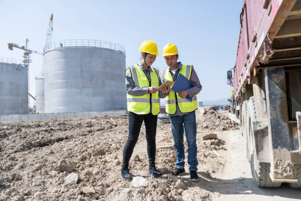 Two engineers work at the construction site of the chemical plant Two young engineers work on the unfinished chemical plant site oil refinery stock pictures, royalty-free photos & images