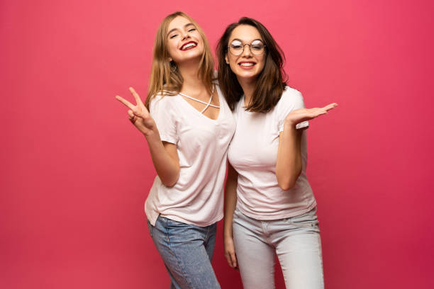 two exited woman having fun and raising hands up. standing on pink background. lucky mood. - friends color background imagens e fotografias de stock