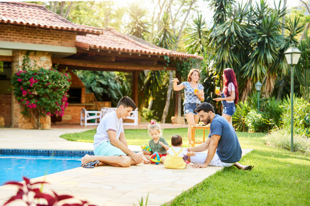 Two families enjoying holidays at a resort Two men sitting by the swimming pool with their kids and two women having conversation in background at a tourist resort airbnb stock pictures, royalty-free photos & images