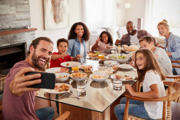 две семьи, принимающие селфи, как они наслаждаются едой дома вместе - ланч стоковые фото и изображения
